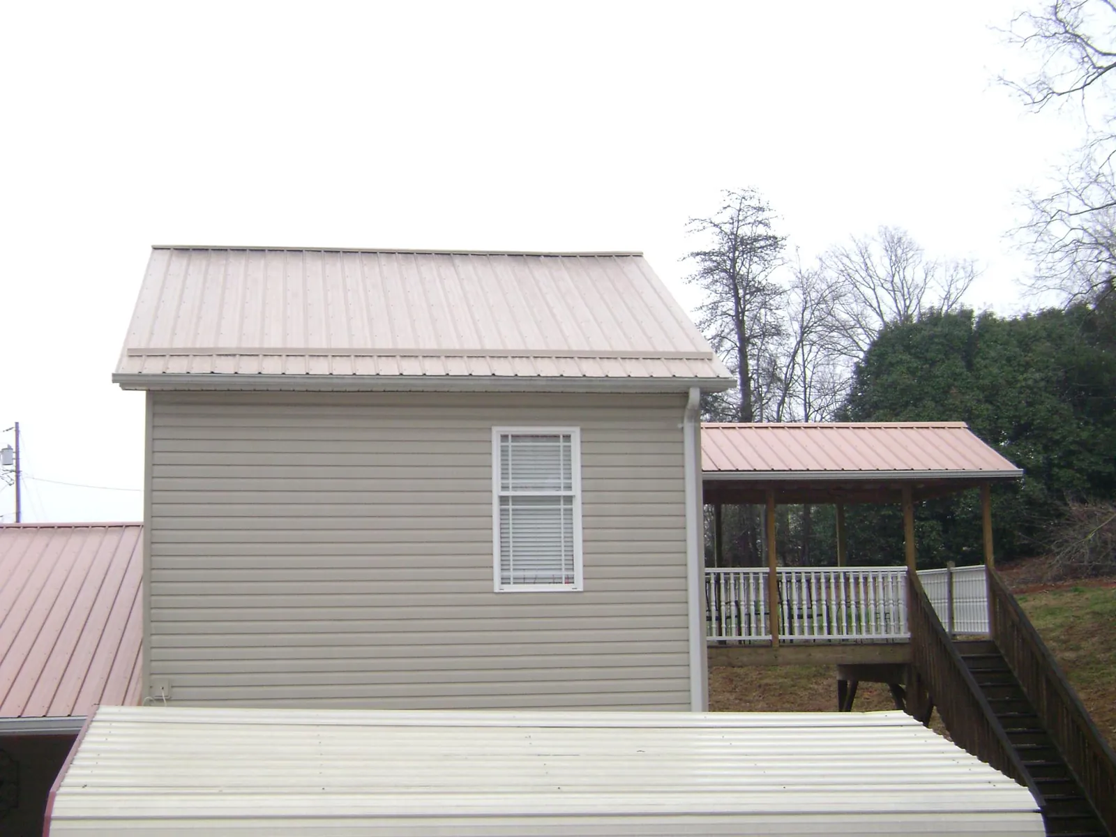 Tan metal roofs on a two story addition and attached porch, from a Roof Replacement job in Saint Marys